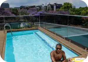 Rooftop pool at Home Suite Hotels Rosebank, framed by jacaranda trees and the Johannesburg skyline