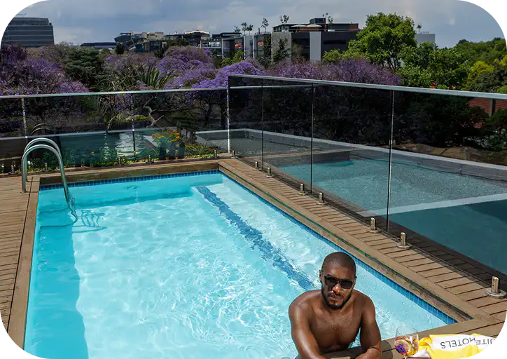 Rooftop pool at Home Suite Hotels Rosebank, framed by jacaranda trees and the Johannesburg skyline